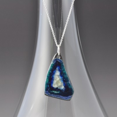 Organic triangle shaped pendant with white center, blues and greens, and crackled glass on a silver chain.